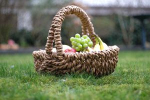 Geflochtener Picknickkorb gefüllt mit Obst auf einer grünen Wiese.